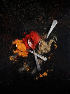 A creative flat lay of colorful spices - red, orange, and brown - with metal spoons on a dark background.